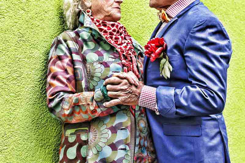 Senior man and woman in bright clothes holding hands and dancing together