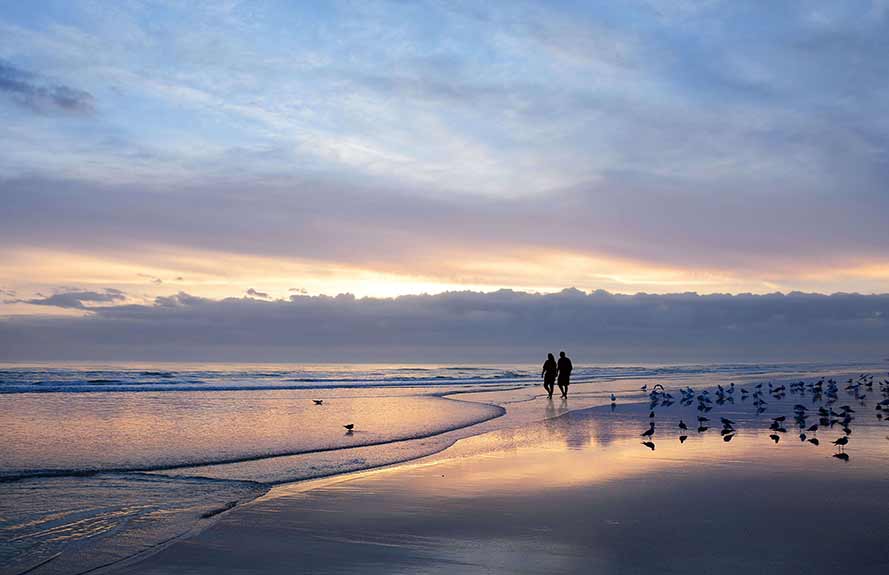 Older couple walking along a deserted beach at sunset