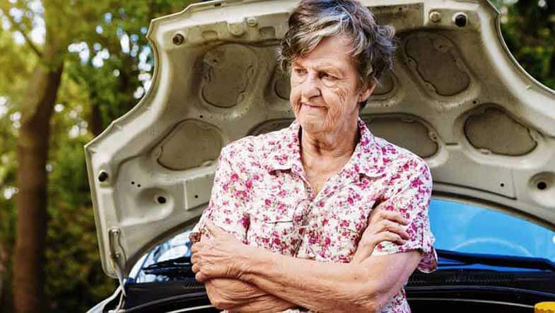 Older woman leaning against a car with unhappy facial expression