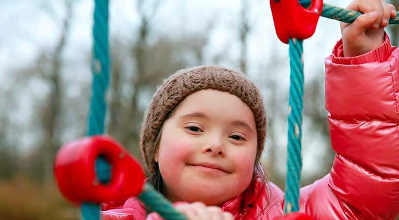 A smiling young girl with Downs Syndrome plays on a swing