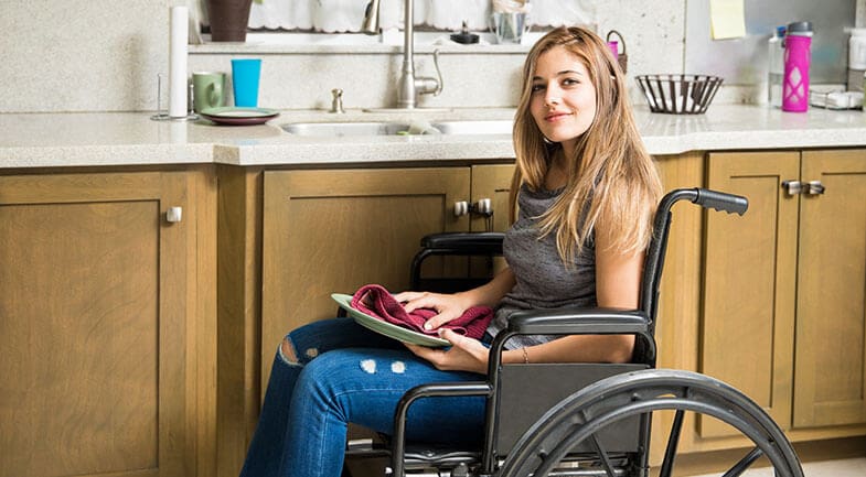 Young girl in a wheelchair drying a plate