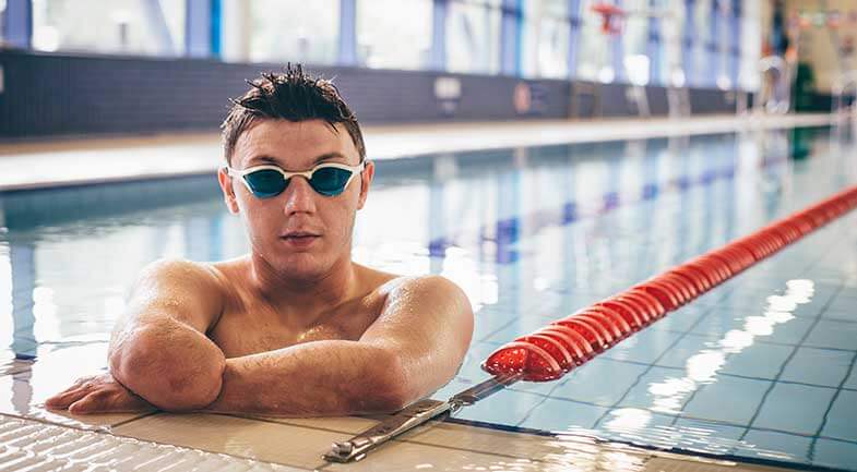 Young man with amputated forearm wearing goggles in a swimming pool