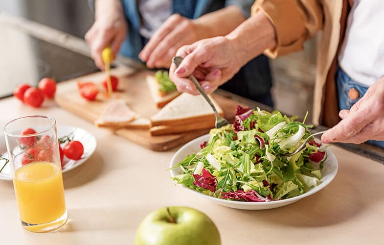 Two elderly people (hands only) preparing a salad