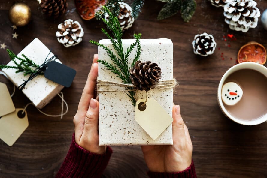 Present wrapped in white speckled paper with pinecone and pine needle decoration