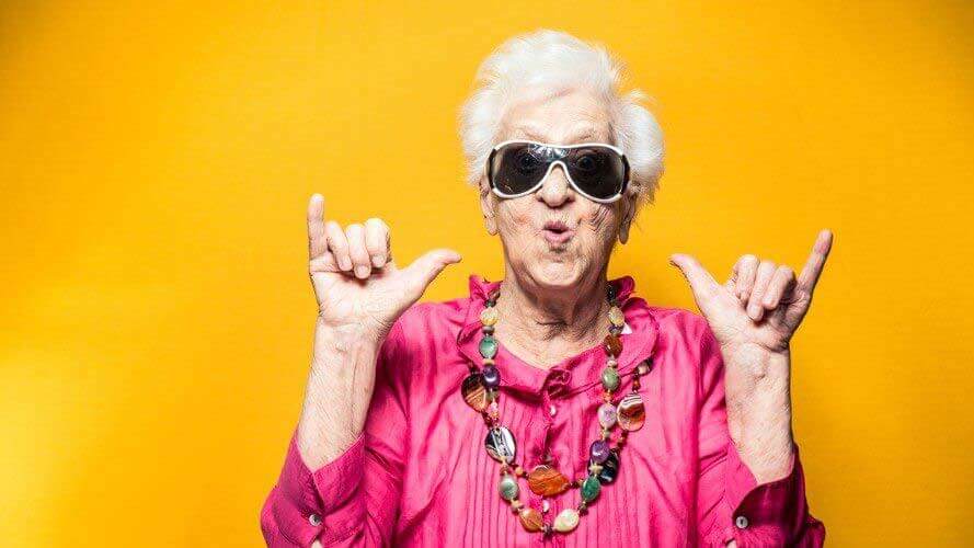 Senior woman in bright pink shirt and black sunglasses, giving the hang-ten sign with her hands!