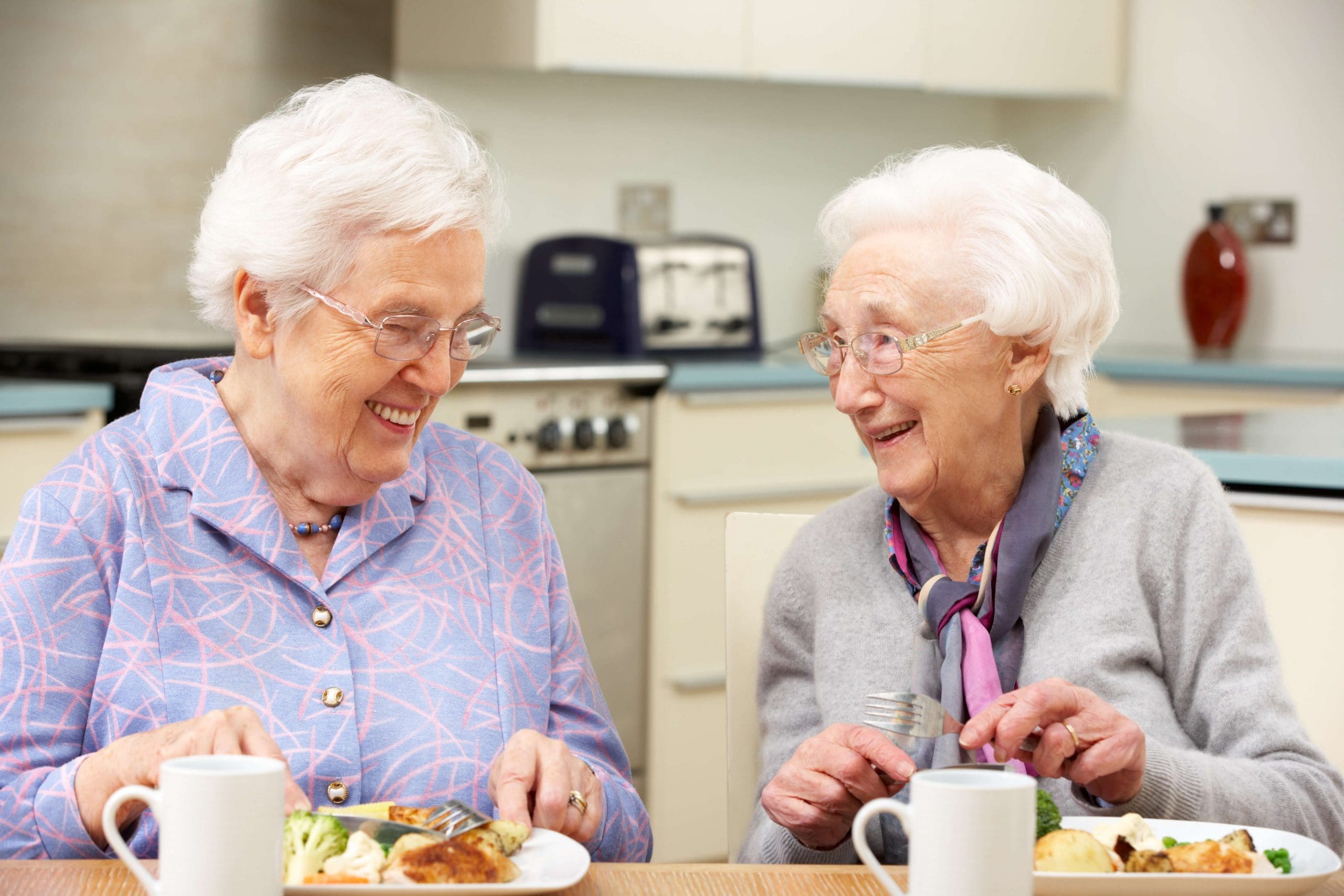 Two elderly ladies laughing together over lunch