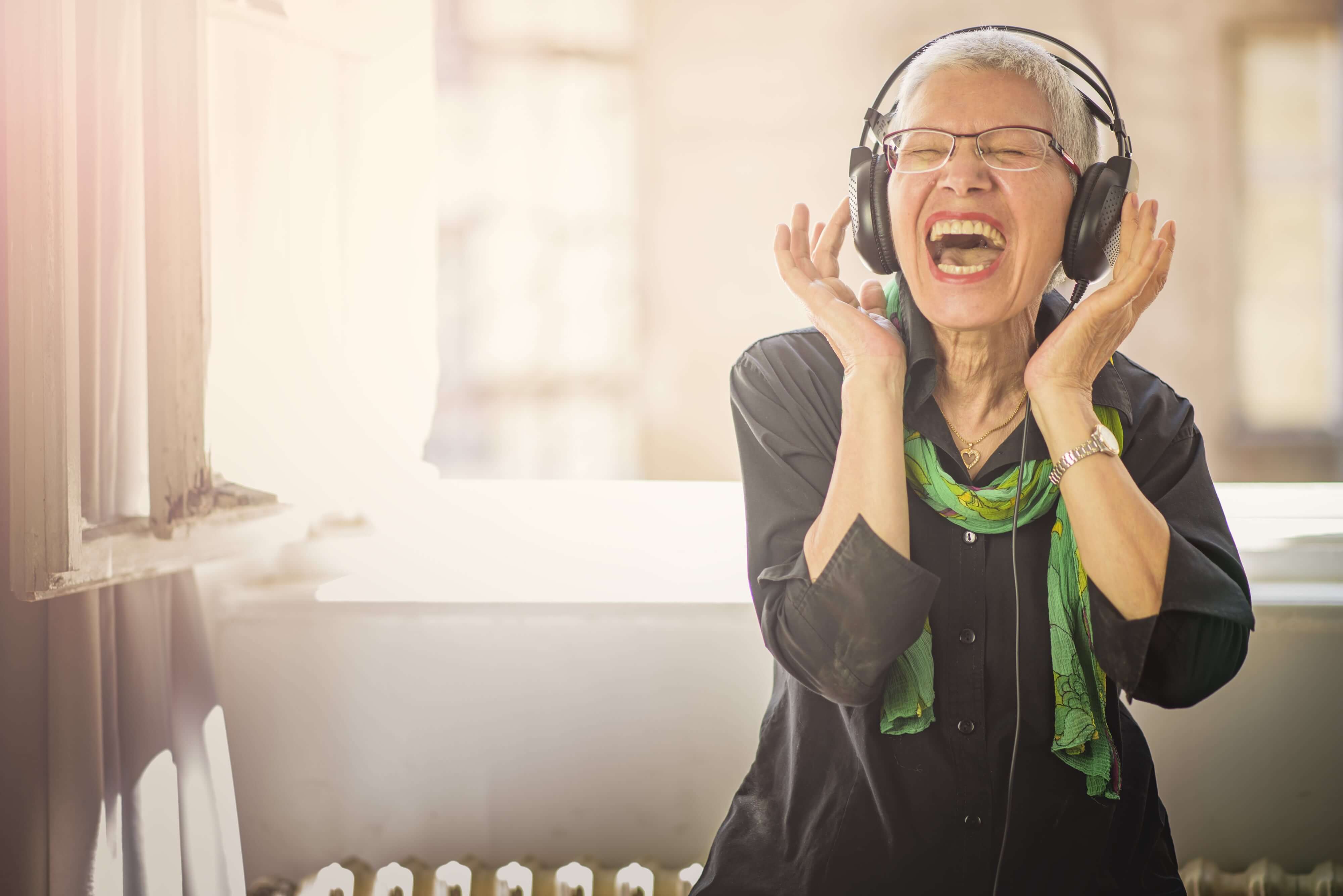 Older woman with headphones on signing loudly and happily