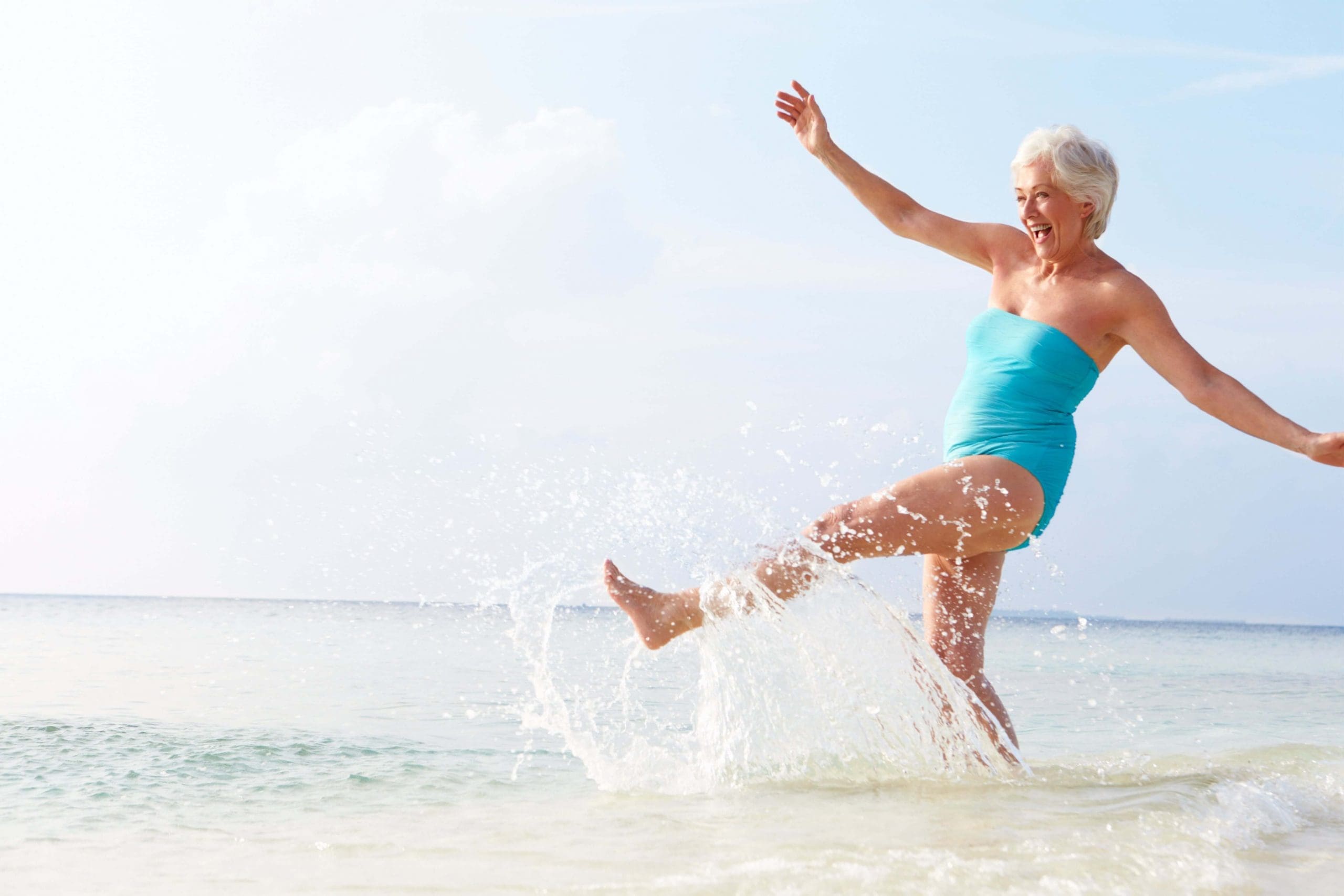 Senior lady wearing blue swimmer and kicking at the waves
