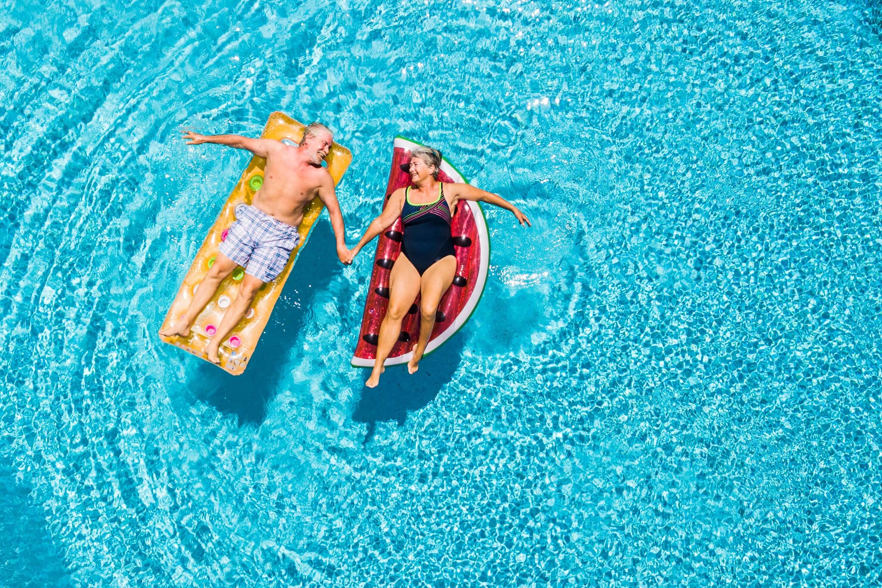 A senior couple floating on blowup beds in a swimming pool