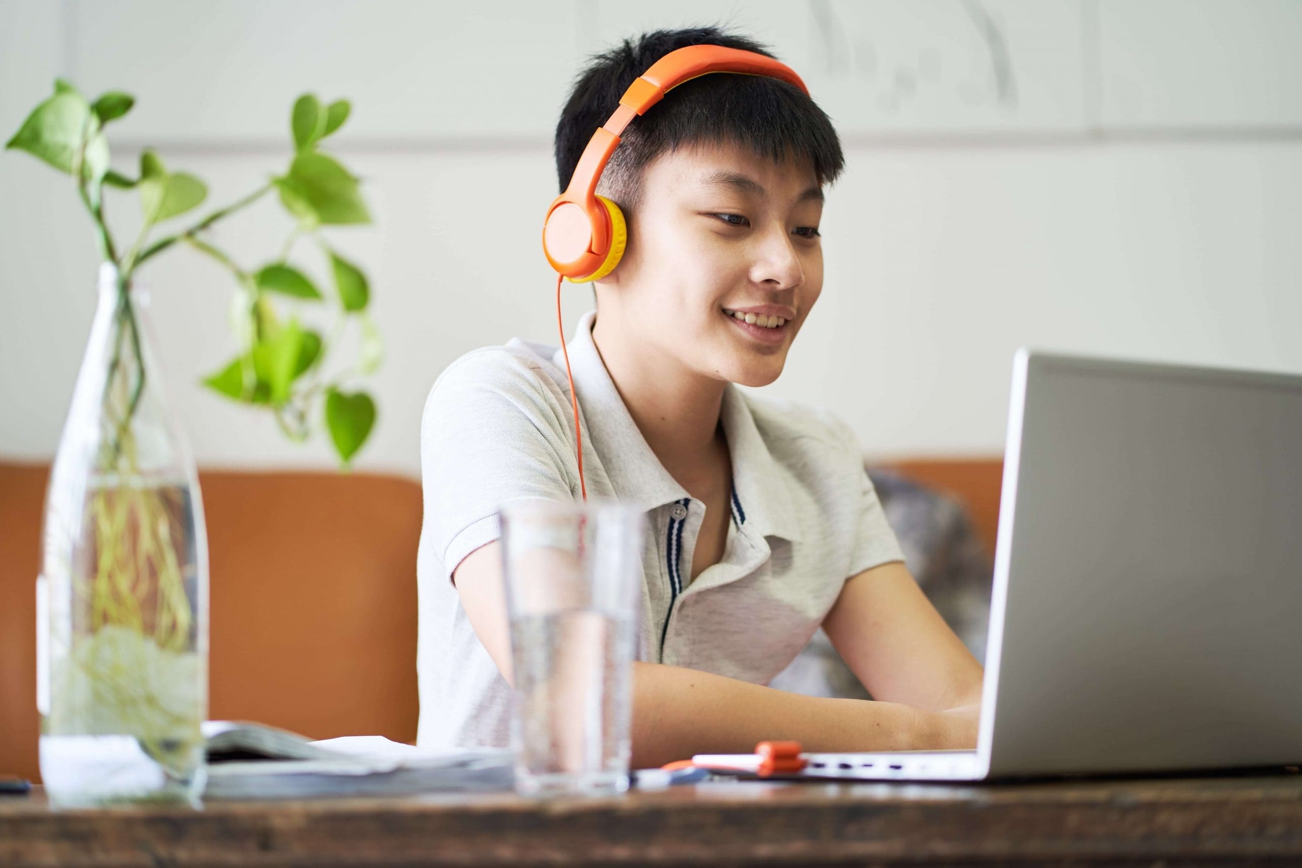 Asian teenage boy wearing headphone and working on a laptop computer