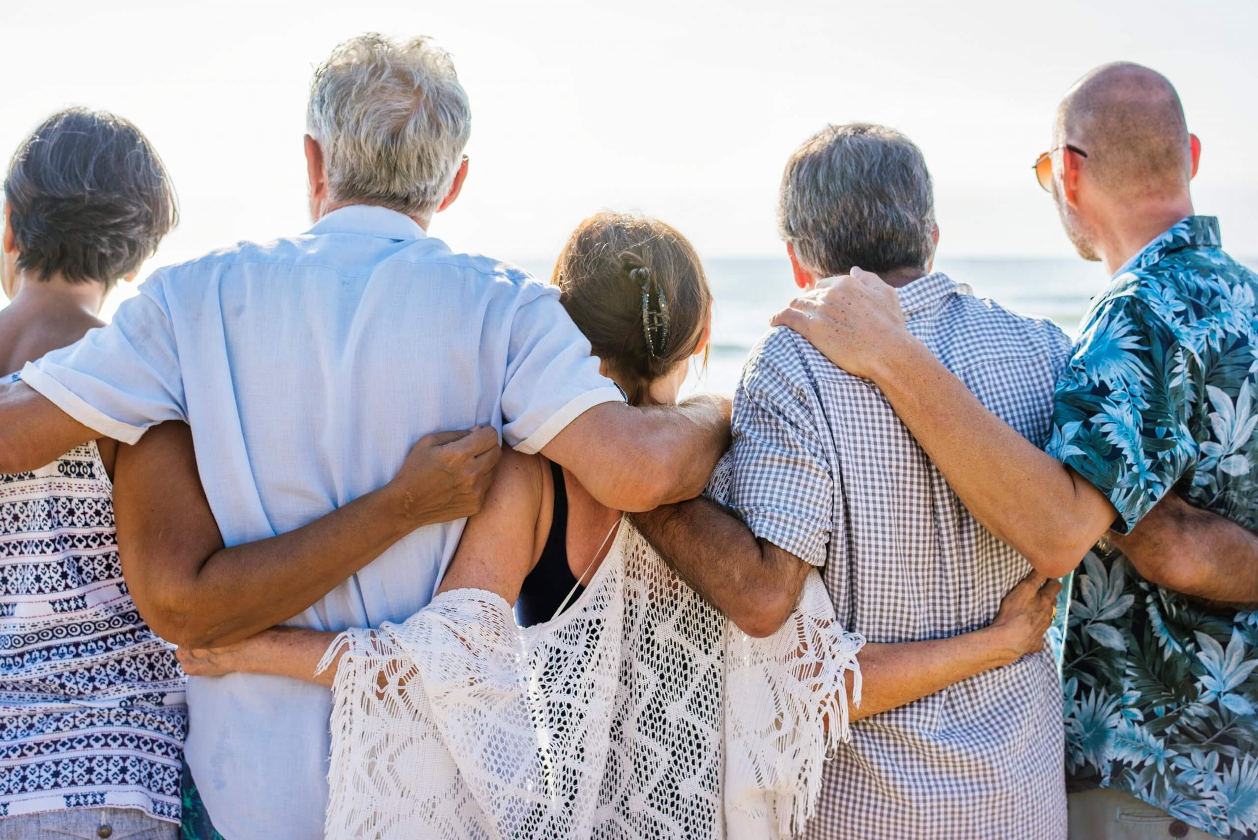 Group of seniors with arms around each other staring out to the ocean