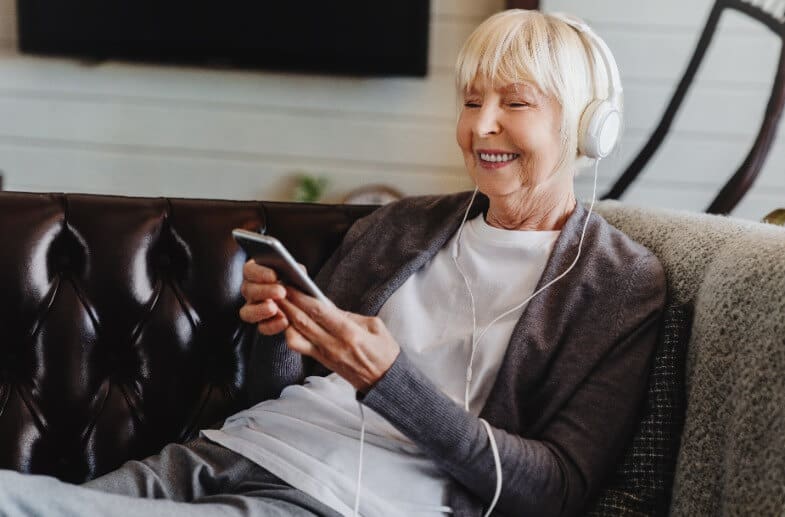 Senior woman smiling while listen to a podcast on her couch