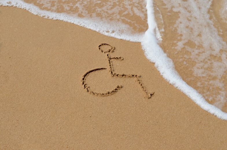 Drawing of a wheelchair icon in the sand with waves rolling in