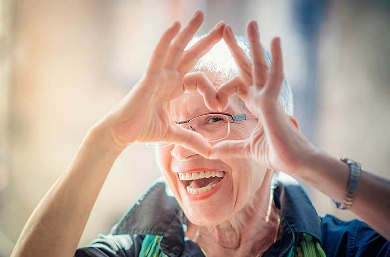 Elderly woman laughing at the camera and making a heart shape with her hands