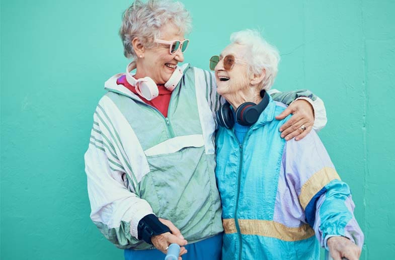 Two elderly female friends, supporting each other and smiling