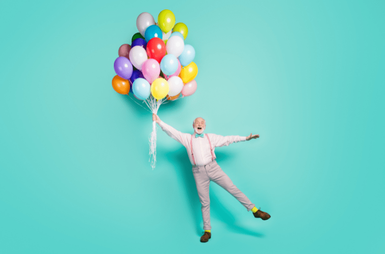 Senior man being carried away with a bunch of brightly coloured balloons